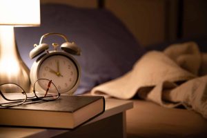 reading glasses resting on a book beside a softly lit lamp representing nighttime relaxation and healthy sleep habits